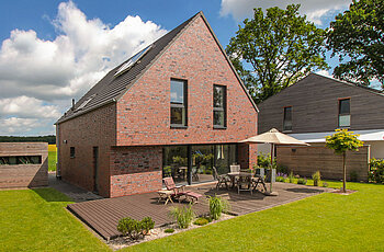 ECO System HAUS – Vario-Haus mit rotem Stein, dunklem Dach und dunklen Fenstern, Terrasse und Garten