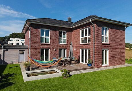 ECO System HAUS – Doppelhaus mit dunkelrotem Stein, dunklem Dach und weißen Fenstern, Terrasse und Garten