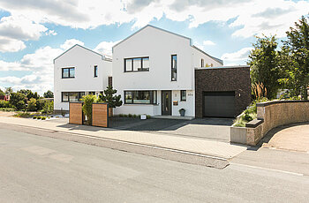 ECO System HAUS – Bauhaus Modern Classic mit weißem Stein und dunklen Fenstern, braungrauer Garage, Straßenansicht