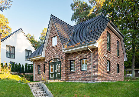 ECO System HAUS – Friesenhaus mit Garten, rotem Stein, dunklen Fenstern und dunklem Dach
