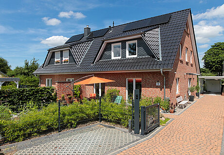 ECO System HAUS – Doppelhaus mit rotem Stein und dunklem Dach, weißen Fenstern und Terrasse
