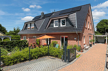 ECO System HAUS – Doppelhaus mit rotem Stein und dunklem Dach, weißen Fenstern und Terrasse