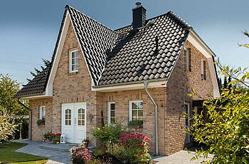 ECO System HAUS – Friesenhaus mit rotbraunem Stein, weißen Fenstern und dunklem Dach