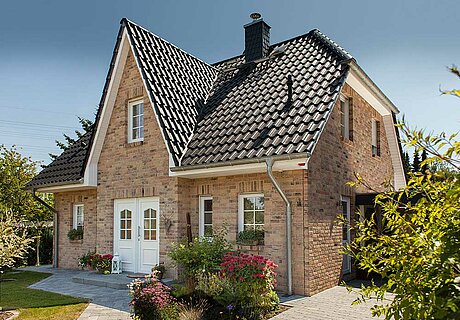 ECO System HAUS – Friesenhaus mit rotbraunem Stein, weißen Fenstern und dunklem Dach