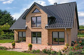 ECO System HAUS – Kapitänshaus mit beigem Stein, dunklen Fenstern, Terrasse und Garten