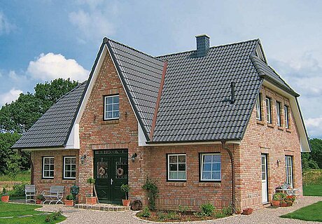 ECO System HAUS – Friesenhaus mit rotem Stein, dunklem Dach und dunkler Tür im Grünen