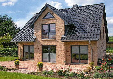 ECO System HAUS – Kapitänshaus mit beigem Stein, dunklen Fenstern, Terrasse und Garten
