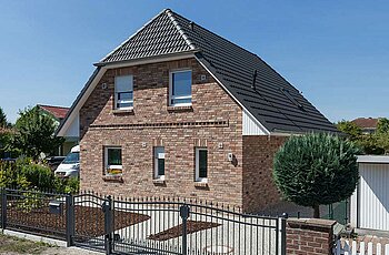 ECO System HAUS – Vario-Haus mit rot-braunem Stein, dunklem Dach und weißen Fenstern, Straßenansicht