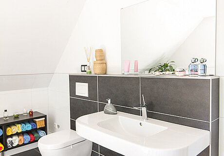 ECO System HAUS – Badezimmer mit dunkelgrauen Fliesen, Waschbecken und WC