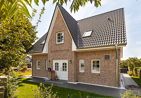 ECO System HAUS – Friesenhaus mit Garten, rotem Stein, hellen Fenstern und dunklem Dach