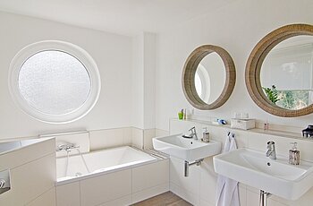 ECO System HAUS – Badezimmer mit braunem Boden und weißen Wänden, Ansicht Badewanne und Waschbecken