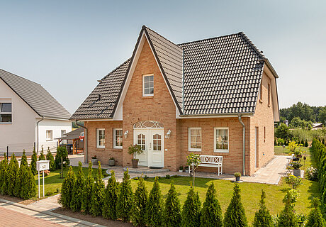 ECO System HAUS – Friesenhaus mit rotem Stein, weißen Türen und Fenstern und dunklem Dach