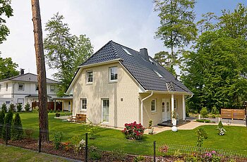 ECO System HAUS – Vario-Haus mit beigem Stein, dunklem Dach und weißen Fenstern und einem Garten