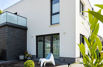 ECO System HAUS – Bauhaus Modern Classic mit dunklem und weißem Stein, dunklen Fenstern und großer Terrasse