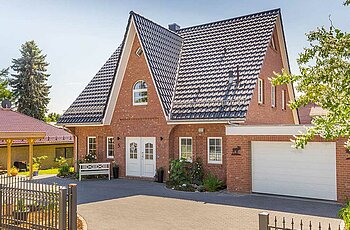 ECO System HAUS – Friesenhaus mit rotem Stein, dunklem Dach, hellen Fenstern und Garage