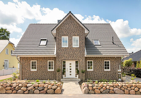 ECO System HAUS – Kapitänshaus mit grau-braunem Stein, dunklem Dach und weißen Fenstern und Türen