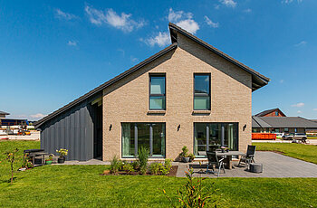 ECO System HAUS – Pultdachhaus mit beigen Stein, dunklem Dach und dunklen Fenstern mit Terasse