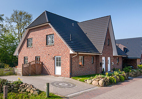ECO System HAUS – Doppelhaus mit rotem Stein, dunklem Dach und dunklen sowie hellen Fenstern