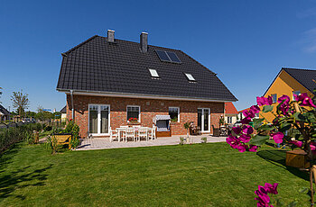 ECO System HAUS – Vario-Haus mit rotem Stein, dunklem Dach und weißen Fenstern, Garten und Terrasse