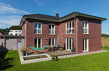 ECO System HAUS – Doppelhaus mit dunkelrotem Stein, dunklem Dach und weißen Fenstern, Terrasse und Garten