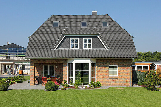 ECO System HAUS – Vario-Haus mit hellrotem Stein, dunklem Dach, weißen Fenstern und großem Garten