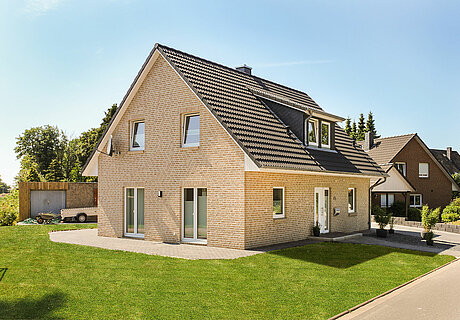 ECO System HAUS – Vario-Haus mit beige-rotem Stein, dunklem Dach, weißen Fenstern und Garten