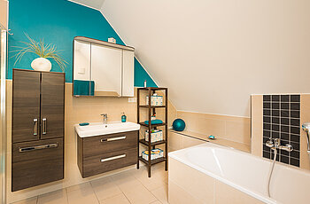 ECO System HAUS – Badezimmer in beige-blau mit braunem Waschtisch und einer Badewanne