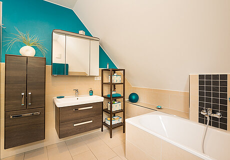 ECO System HAUS – Badezimmer in beige-blau mit braunem Waschtisch und einer Badewanne