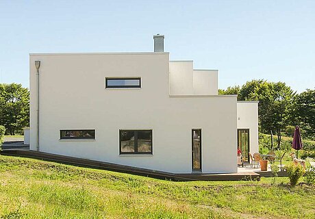 ECO System HAUS – Bauhaus Modern Classic mit weißem Stein und dunklen Fenstern im Grünen