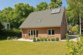 ECO System HAUS – Vario-Haus mit rotem Stein, dunklem Dach, weißen Fenstern und Garten