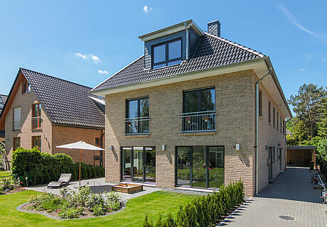 ECO System HAUS – Doppelhaus mit hellem Stein, dunklem Dach und dunklen Fenstern mit Terrasse und Garten