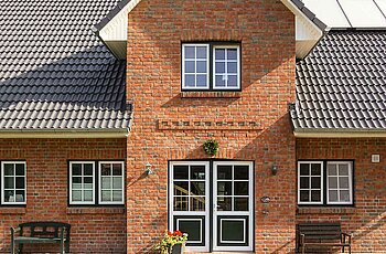 ECO System HAUS – Kapitänshaus mit rotem Stein, dunklem Dach und einem gepflasterten Weg zum Haus