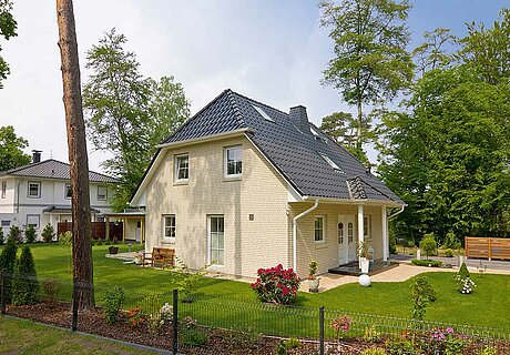 ECO System HAUS – Vario-Haus mit beigem Stein, dunklem Dach und weißen Fenstern und einem Garten