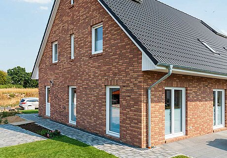 ECO System HAUS – Doppelhaus mit rotem Stein, dunklem Dach und hellen Fenstern