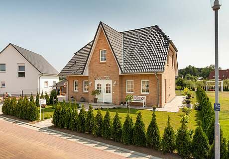 ECO System HAUS – Friesenhaus mit rotem Stein, weißen Türen und Fenstern und dunklem Dach