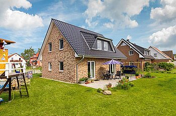 ECO System HAUS – Vario-Haus mit rot-beigem Stein, dunklem Dach, weißen Fenstern, Terrasse und Garten