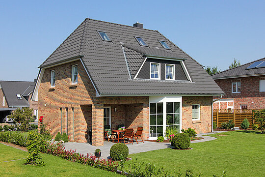 ECO System HAUS – Vario-Haus mit hellrotem Stein, dunklem Dach, weißen Fenstern und großem Garten
