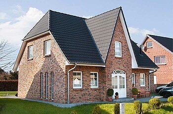 ECO System HAUS – Friesenhaus mit rotem Stein, dunklem Dach und weißen Fenstern