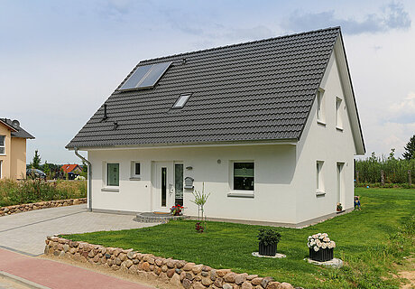 ECO System HAUS – Vario-Haus mit weißem Stein, weißen Fenstern, dunklem Dach und Vorgarten