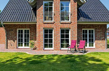 ECO System HAUS – Kapitänshaus mit rotem Stein, dunklem Dach, weißen Fenstern und einem Garten mit Terrasse