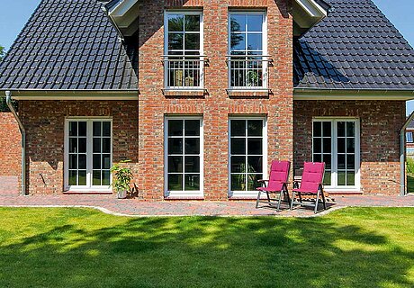 ECO System HAUS – Kapitänshaus mit rotem Stein, dunklem Dach, weißen Fenstern und einem Garten mit Terrasse