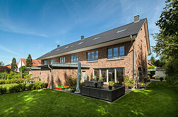 ECO System HAUS – Mehrfamilienhaus mit rotem und dunklem Stein und dunklem Dach, Gartenansicht