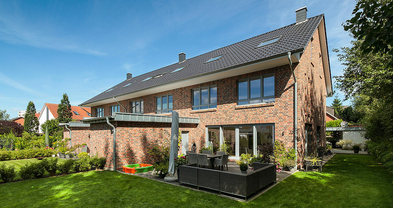 ECO System HAUS – Mehrfamilienhaus mit rotem und dunklem Stein und dunklem Dach, Gartenansicht