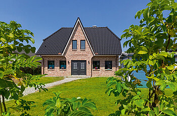 ECO System HAUS – Friesenhaus mit rotem Stein, dunklem Dach und dunklen Fenstern und mit großem Garten