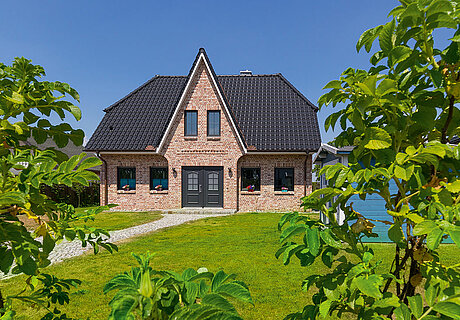 ECO System HAUS – Friesenhaus mit rotem Stein, dunklem Dach und dunklen Fenstern und mit großem Garten